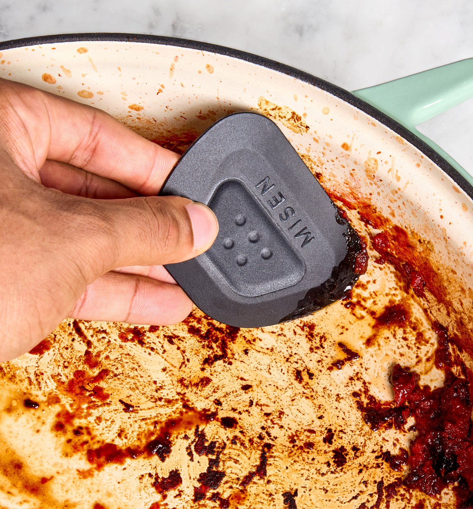 Misen pan scraper cleaning burnt food residue from enameled cast iron skillet